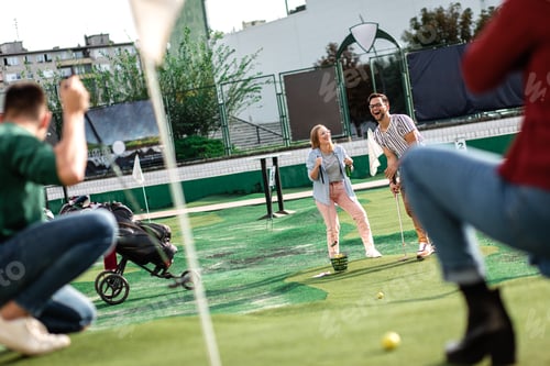 Preview: Group of smiling friends enjoying together playing mini golf in the city.