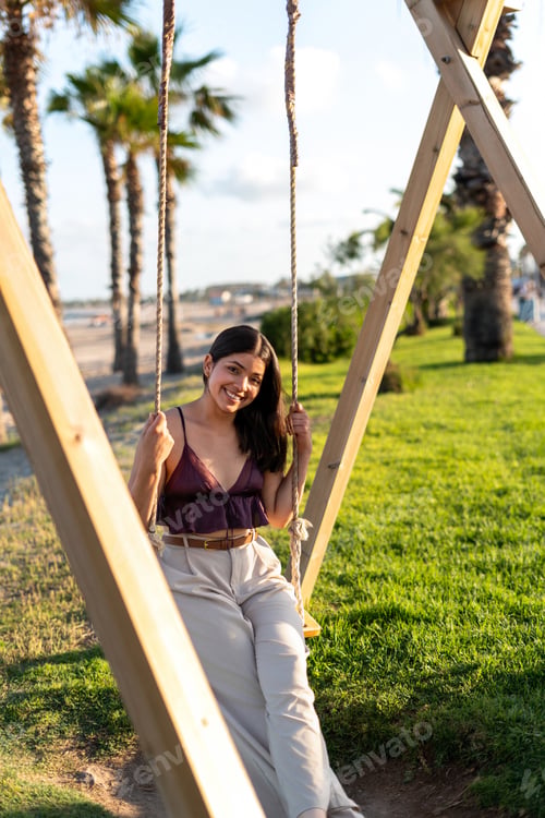 Preview: Beautiful young woman relaxing on a swing in a park near the beach