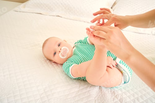 Preview: Baby on the bed in a green dress lies on a white bed.