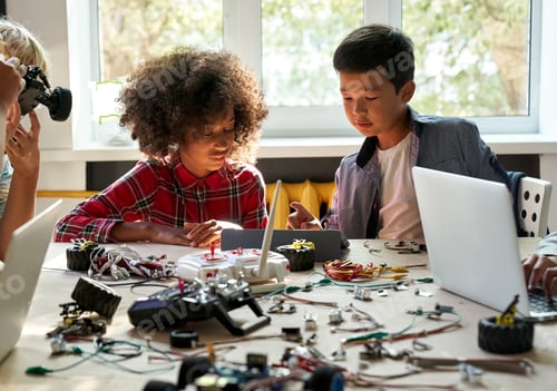 Preview: Asian school kid boy helping African girl using tablet programming robotic cars.