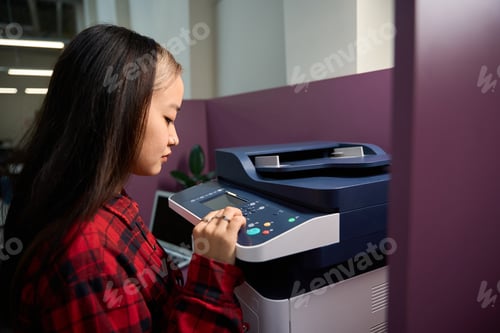 Preview: Young asian female IT employee pressing button on printer in coworking office