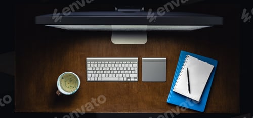 Preview: Computer, notepads and a cup of tea on the desktop at night, top view.