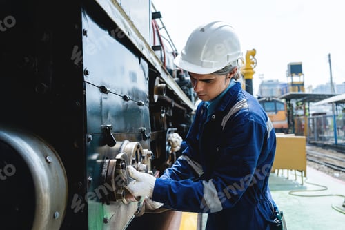 Preview: A man in a blue and white uniform is working on a train engine.