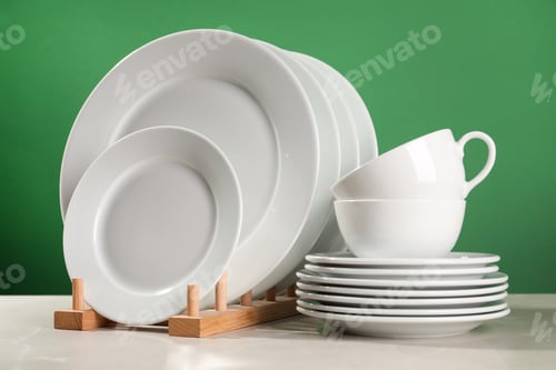 Preview: Set of clean dishware on white table against green background