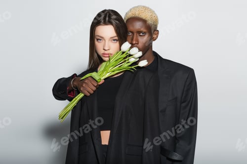 Preview: african ameican man with bleached hair holding white tulips near young brunette woman on grey