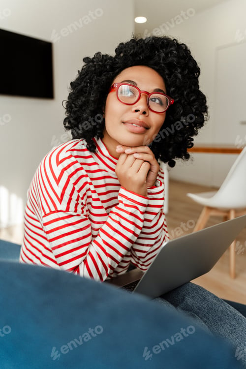 Preview: Attractive, beautiful curly African American woman wearing eyeglasses sitting on comfortable sofa