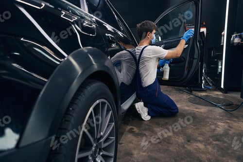 Preview: Man in repair workshop washing car window during car valeting