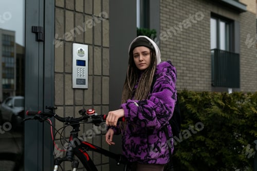 Preview: Stylish informal woman with dreadlocks wearing a purple jacket rides a bicycle