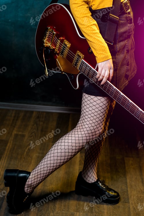 Preview: Close-up photo of young hipster woman legs and red guitar in neon lights. 90s style concept.