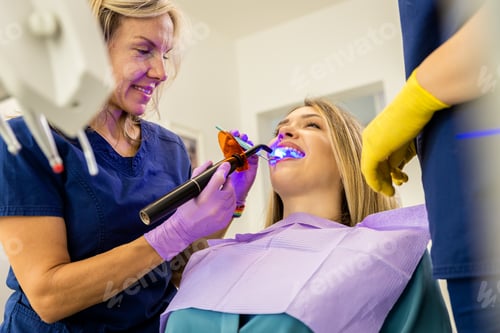 Preview: Female dentist with assistant working in dental clinic examining patient teeth.