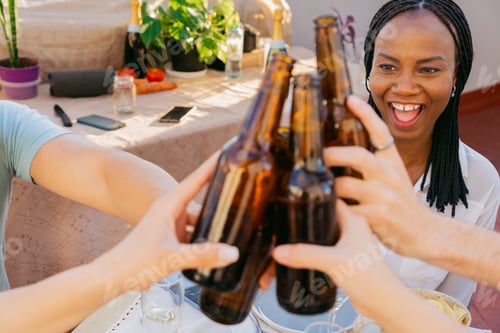 Preview: Happy Black woman toasting with beer on a terrace with friends