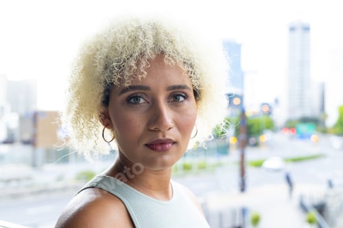 Preview: Young biracial woman with blonde curls and brown eyes looks ahead in modern office