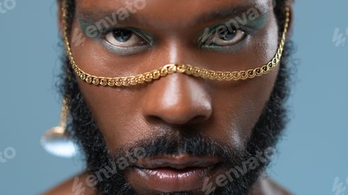 Preview: Black gay man with blue eyeshadow and golden accessory on face