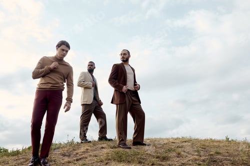Preview: Stylish men in autumn attire posing in a scenic field under a cloudy sky