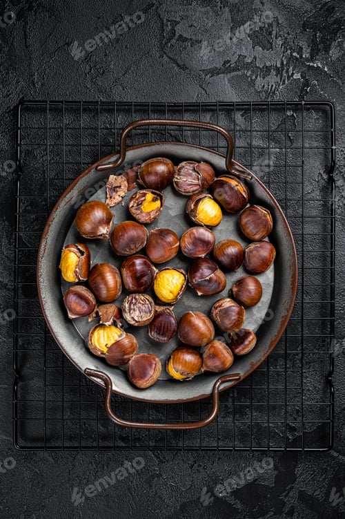 Preview: Cracked roast chestnuts served in a tray. Black background. Top view