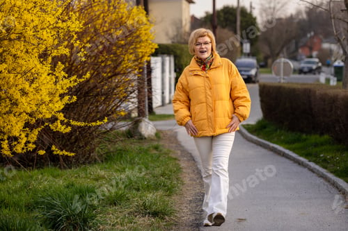 Preview: A young beautiful woman walks through the city past a blooming forsythia.