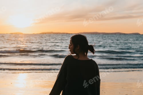 Preview: Woman in the beach looking a colorful sunset during a bright day with copy space