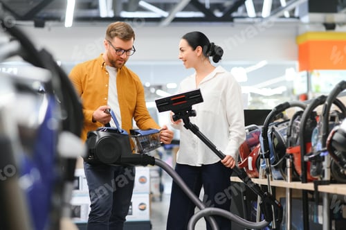 Preview: couple crouching and looking at vacuum cleaner they want to buy. Tech store interior