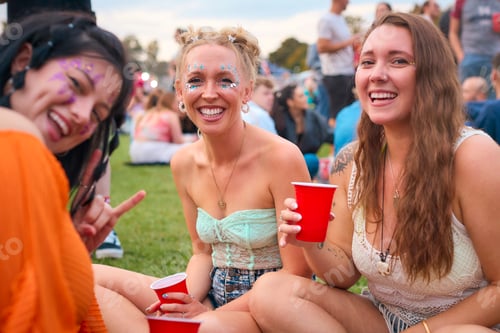 Preview: Portrait Of Three Female Friends Wearing Glitter Having Fun At Summer Music Festival Holding Drinks