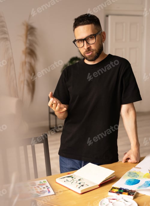 Preview: The artist discusses his work with an interlocutor. A young man standing over a desk in a workshop.