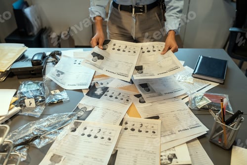 Preview: Hands of female investigator holding criminal profiles over desk with documents
