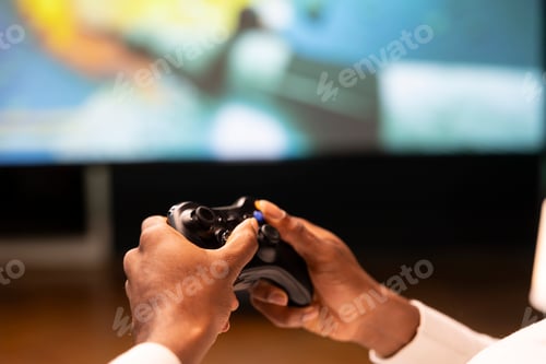 Preview: Close up shot of controller held by gamer sitting in front of large television set