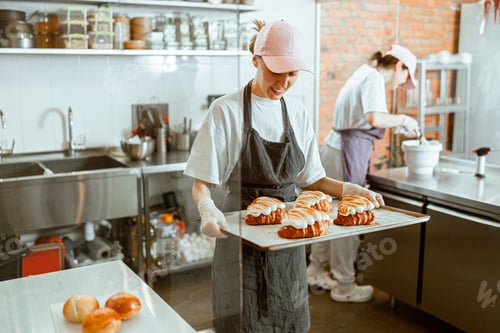 Preview: Smiling woman holds tray with delicious croissants decorated with burnt cream in craft bakery
