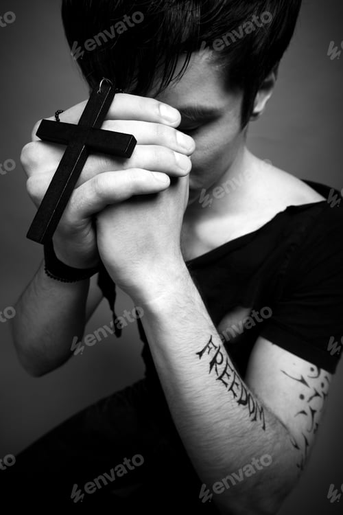 Preview: Young man in modern black clothing holding big black cross in hands