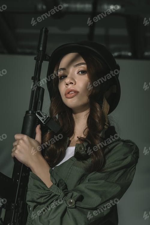 Preview: beautiful girl posing in military helmet with rifle, on grey with shadows