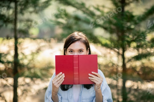 Preview: Curious eyes peek over a red book held by a person in a light blue shirt, creating a playful
