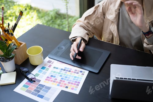 Preview: Young woman working with graphic tablet and color swatch in office.
