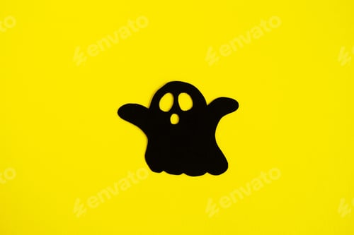 Preview: Holiday decorations for Halloween. Black paper ghost on a yellow background, top view.