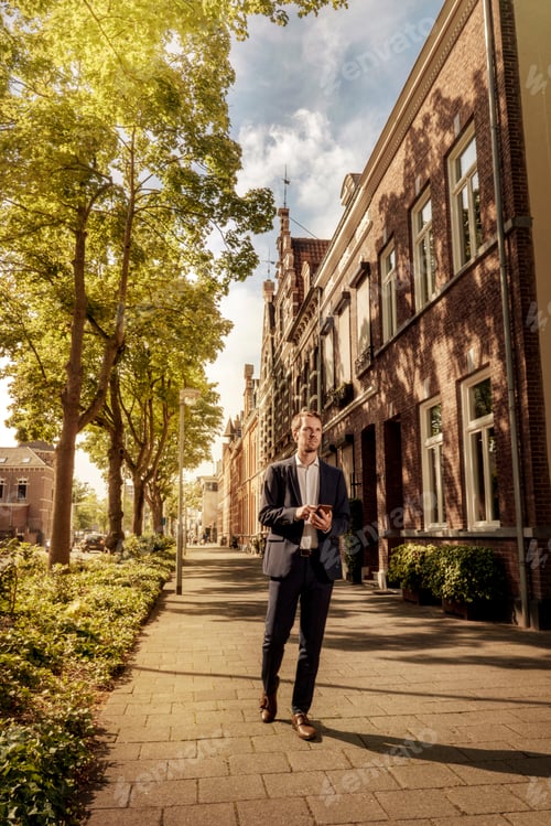 Preview: Netherlands, Venlo, businessman with cell phone walking on pavement