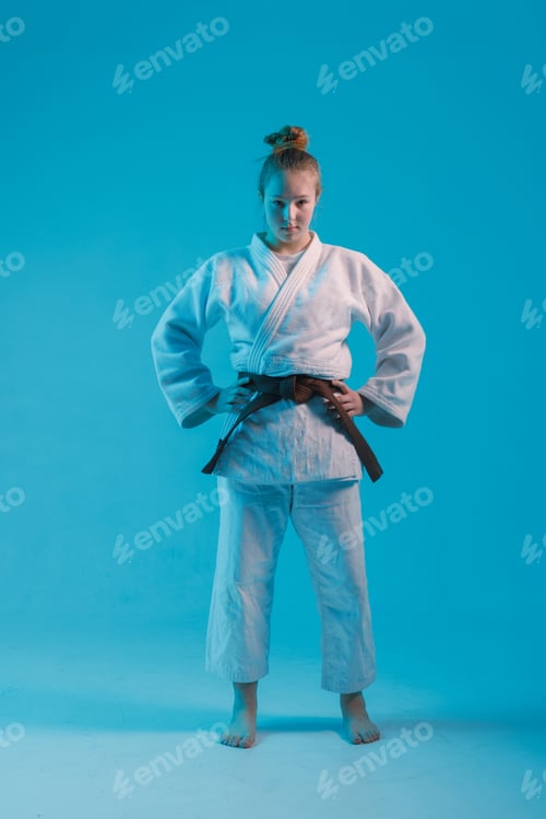 Preview: girl judoka in a white kimano with a black belt on a blue background, studio photo