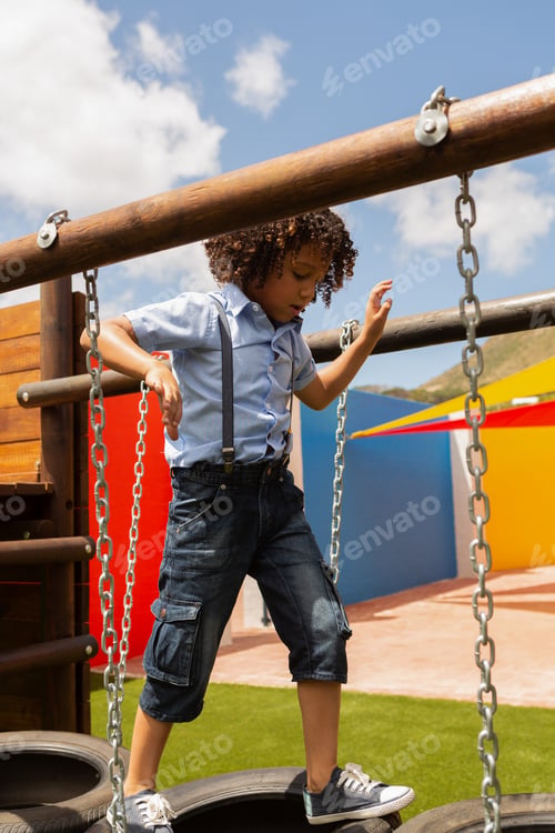 Preview: Mixed-race schoolgirl walking on a hanging tire in the school playground on a sunny day