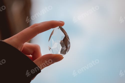 Preview: Teardrop-shaped crystal in a female hand in the light blue background