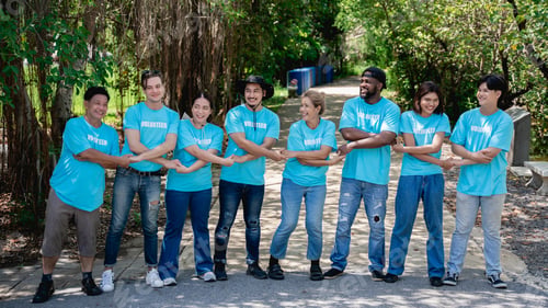 Preview: Group of volunteers for charity join hands and arm around in the forest park area.