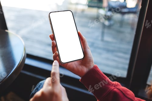 Preview: Mockup image of a woman holding and touching on mobile phone with blank desktop screen in cafe