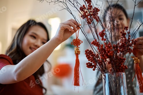 Preview: Close up of Chinese mother and daughter hanging ornaments for New Year celebration at home.