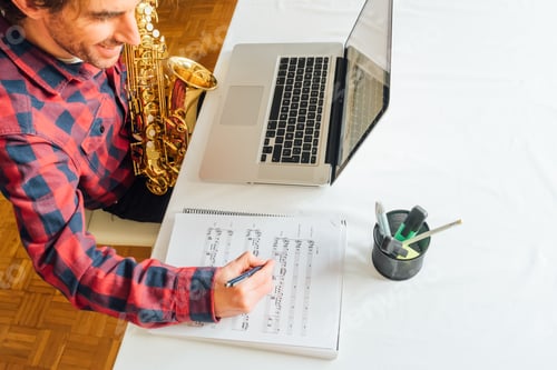Preview: Man making notes on sheet music while taking his saxophone online course