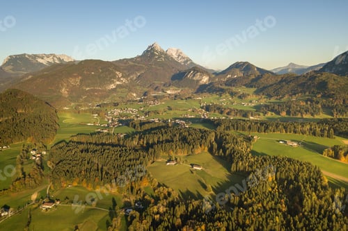 Preview: Aerial view of green meadows with villages and forest in austrian Alps mountains.