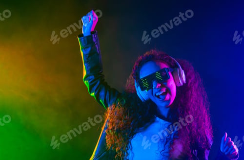 Preview: Happy woman in headphones dancing in neon light, smoke background. Z generation