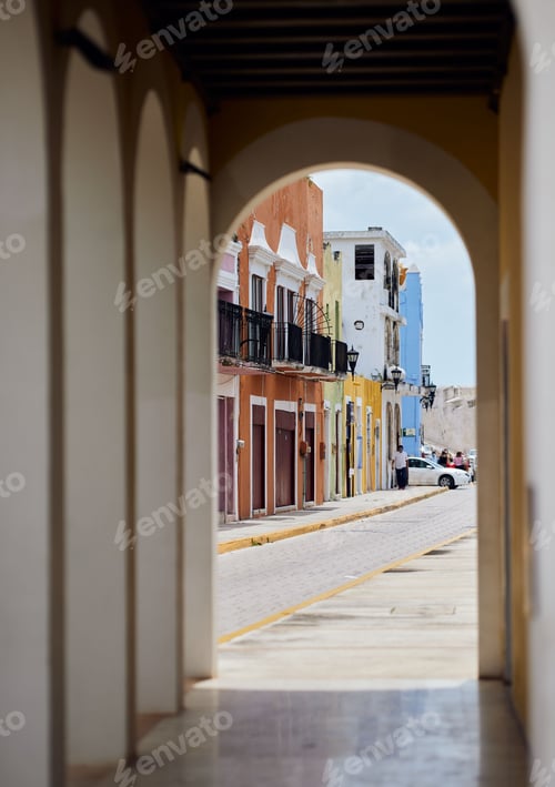 Preview: Narrow street between to old buildings seen through an arched door on a sunny day