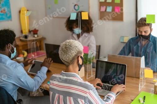 Preview: Young multiracial people using computer in co-working creative space while wearing face mask