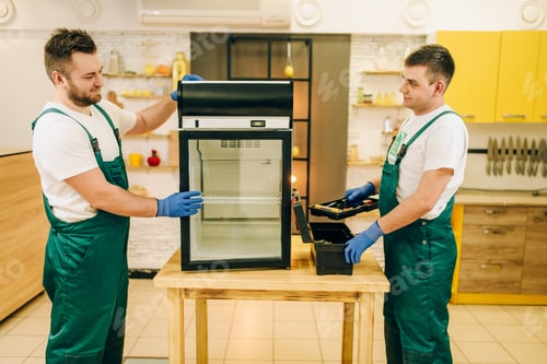 Preview: Two workers in uniform repair refrigerator at home