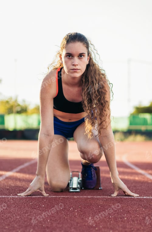 Preview: A female athlete getting ready to run on an athletics track.