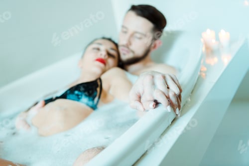 Preview: selective focus of handsome man and attractive brunette woman holding hands while lying in bathtub