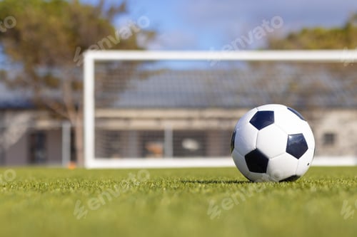 Preview: A soccer ball is resting on green grass with goal in background, copy space, on field outdoors