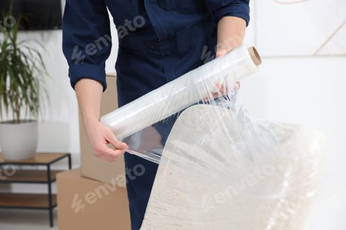 Preview: Male mover with stretch film wrapping armchair in house, closeup