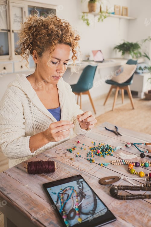 Preview: Woman at home making beads jewels using instructions online on a tablet. Alternative job